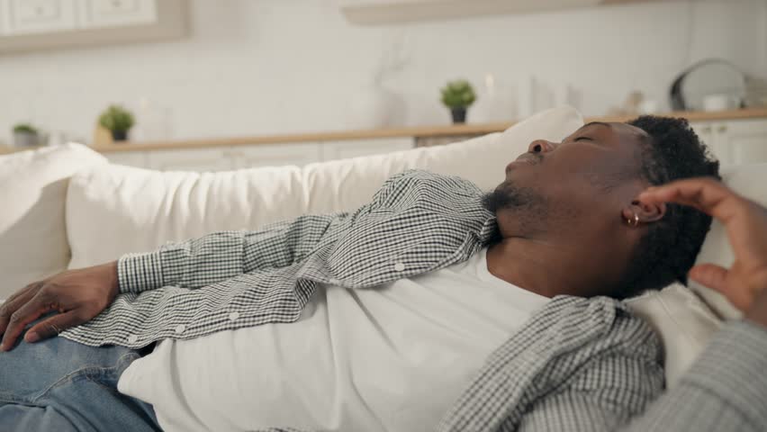 Adult African American man sleeping on couch in weekend, afternoon nap, relax. Recovery of energy, daytime sleep, young black guy resting after hard work day, snoring, REM and non-REM sleep periods
