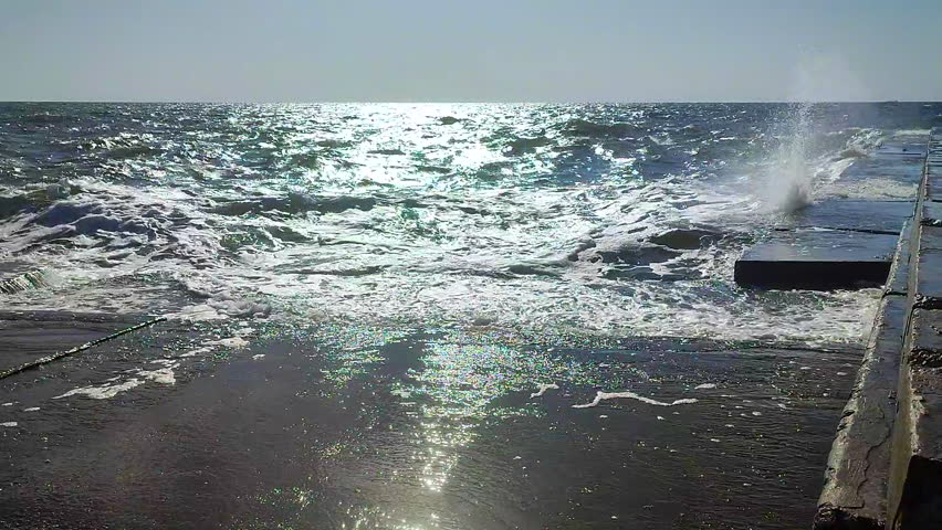 Storm. Storm at sea. Large high sea waves with white foam hitting concrete pier wall and splashing on hot sunny summer day. Stormy sea weather. Rough sea. Shore and waves. Nature. Natural background