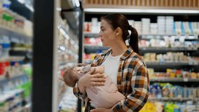 A brunette girl in a plaid shirt holds her infant child in her arms and looks at the goods on the counter in the dairy department of a supermarket - Powered by Shutterstock - Get 15% off with code: PIKWIZARD15