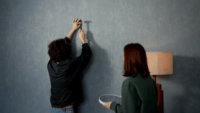 Confident brunette guy hammers a nail into the wall and hangs a clock with the support of his girlfriend in a modern apartment - Powered by Shutterstock - Get 15% off with code: PIKWIZARD15