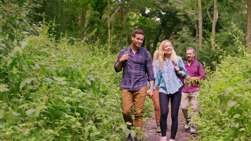 Mid adult couple on hike walking along path through trees with mature friends - shot in slow motion