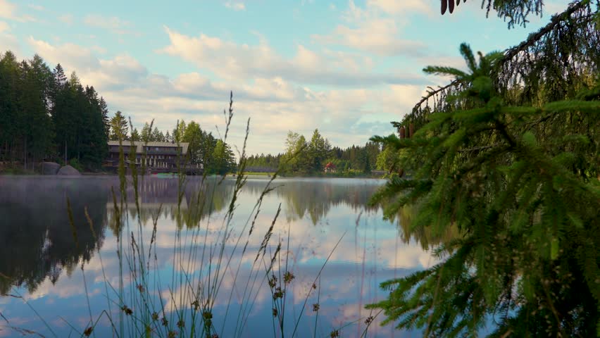 Mesmerizing atmosphere of  early morning. A view through  grass to a small lake. Fog drifts across  water. A small house in  distance. Fichtelseemoor.  Bayern. Germany