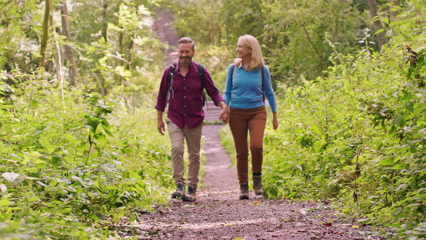 Loving mature couple walking along path through trees holding hands on hike - shot in slow motion