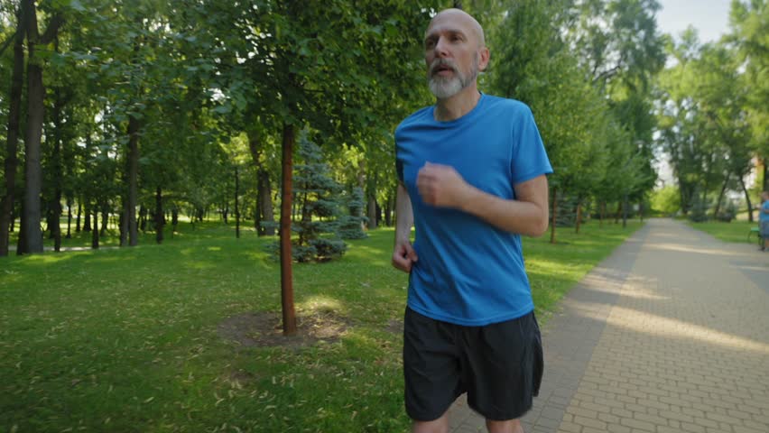 Active motivated athletic fit middle aged male runner suffering from knee injury, holding and massaging kneecap, trying to relieve pain while practicing outdoor jog workout.