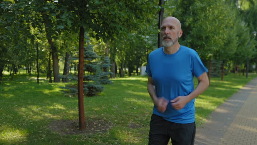 Active handsome fitness middle aged male runner in sportswear answering emergency phone call, shocked by news and running faster while practicing morning jog in public park.