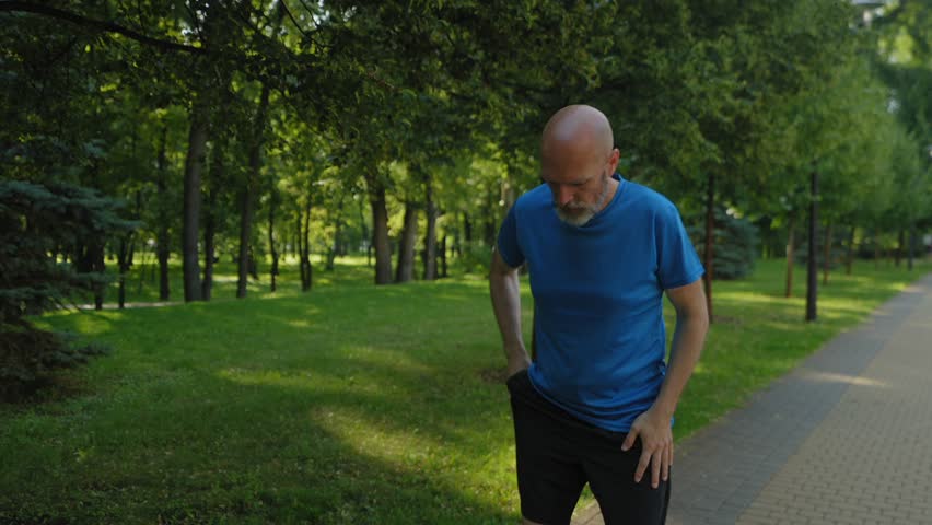 Active handsome fitness middle aged male runner in sportswear answering emergency phone call, shocked by news and running faster while practicing morning jog in public park.