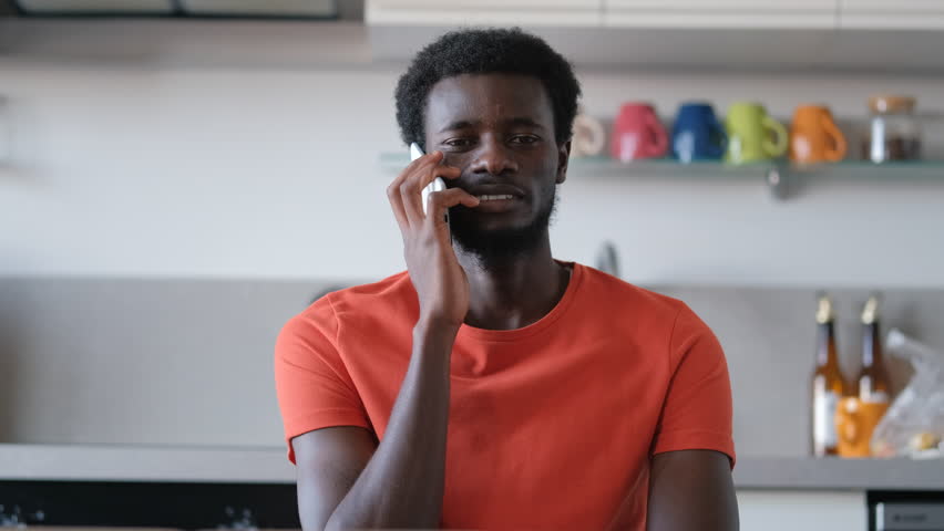 An African man enjoys a pleasant conversation on the phone while relaxing at home. He smiles and chats with a friend. Daily life, communication, and modern lifestyles concepts. 4k