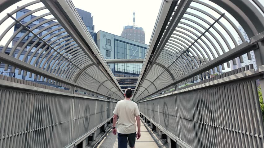 A forward dolly shot following a pedestrian walking on an overpass near the Holland Tunnel in lower Manhattan on a summer day.  	