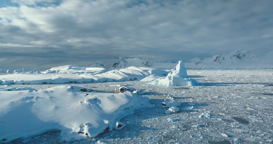Aerial view wild Arctic mountain winter landscape. Snow covered frozen polar ocean, icebergs, glacier under blue sky. Discover beauty of South Pole. Antarctica travel and exploration. Drone panorama