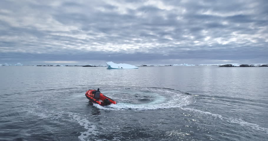 Man riding zodiac boat make circle in water. Motorboat going around making white foam waves. Antarctica polar ocean coastline bay. Icebergs in background. People enjoy Antarctic travel and exploration