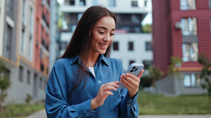 Smiling young woman using smartphone outdoors. Urban city technology lifestyle.