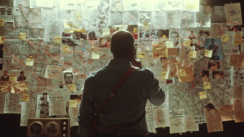 African American detective thoughtfully examining connections and clues on evidence board covered with maps, photos and documents linked by red strings. Back view, zoom-out shot