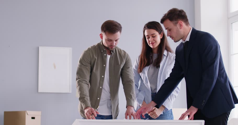 Young happy smiling couple signing a contract with real estate male agent and shaking hands making a deal happy to buy a property. Joyful excited family ready to become homeowners. 4k video.