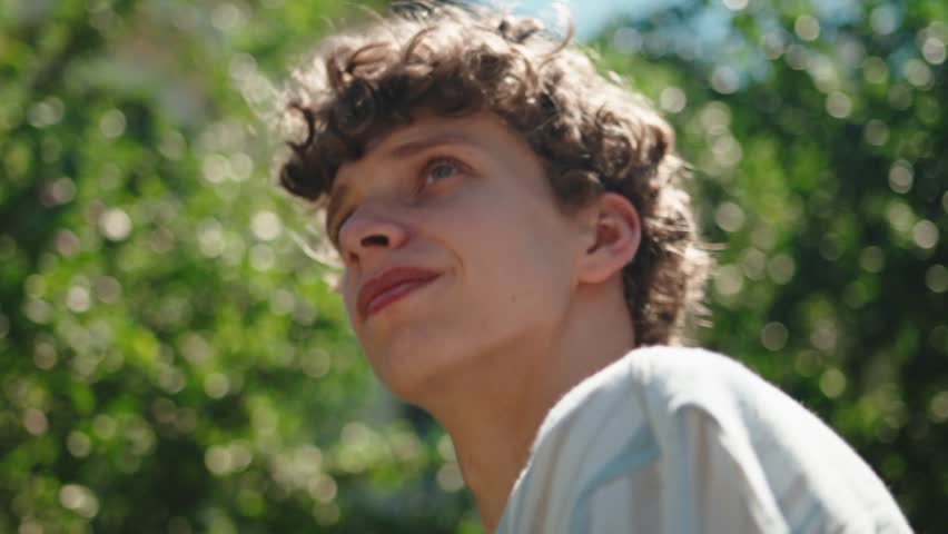 Close-up ethnic male student happy inspired face. Portrait caucasian teenage man young adult pensive guy stands in city on street background of sunset sun dreaming thinking enjoying rays, smiling 