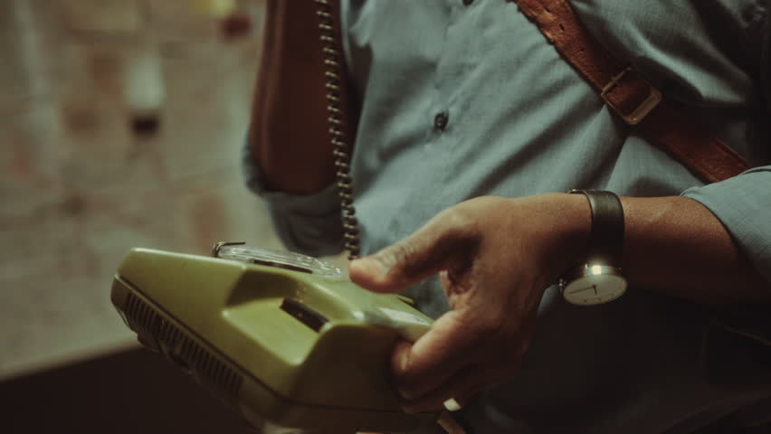 Mature African American detective holding vintage telephone and discussing investigation of criminal case on the call when working late in office. Tilt-up, close-up shot
