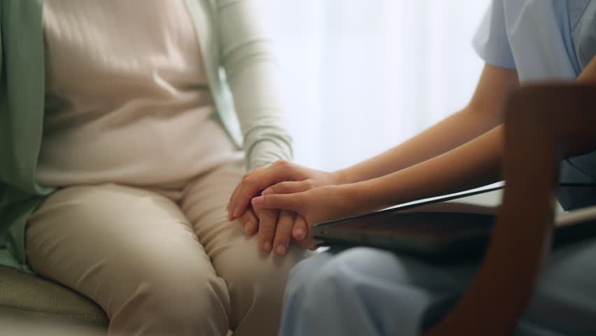 Asian woman caregiver holding hand and consoling elderly patient. Psychiatrist or nurse take care senior woman at nursing home. Home medical caregiving, mental health and healthcare insurance concept.
