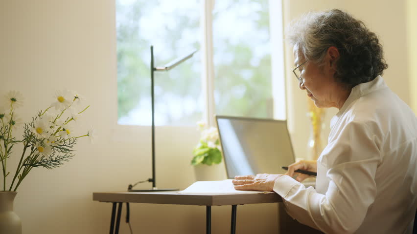 Asian senior mature woman using laptop computer with internet for e-Learning study or business work on desk at home. Elderly people smart life with wireless technology and digital gadget device.