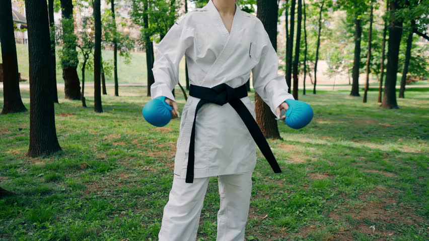 outdoors in the park in sunny weather young karate girl dressed in blue combat boots and gloves practicing techniques