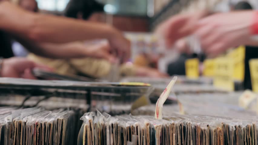 People browsing vinyl records in a music store, surrounded by retro albums in physical format