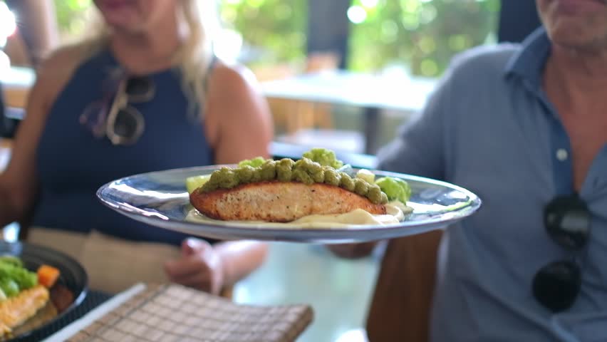 Man puts down plate with salmon and vegetables served on top of a potato puree 