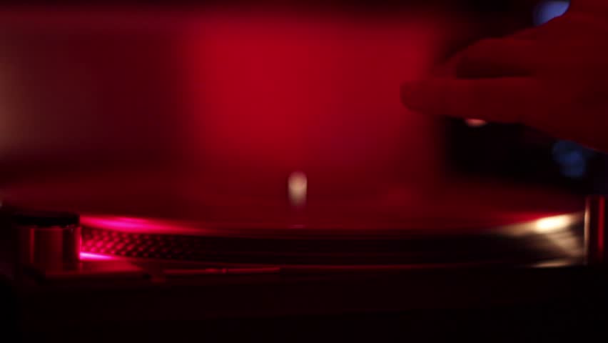 DJ hand places stylus on a turntable vinyl record scratches platter in nightclub