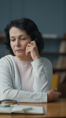 Sad single senior woman sitting area at home, aging and retiring, vertical video, portrait. Grandmother thinking about future, charming brunette lady in old age, aged mother missed children, widow