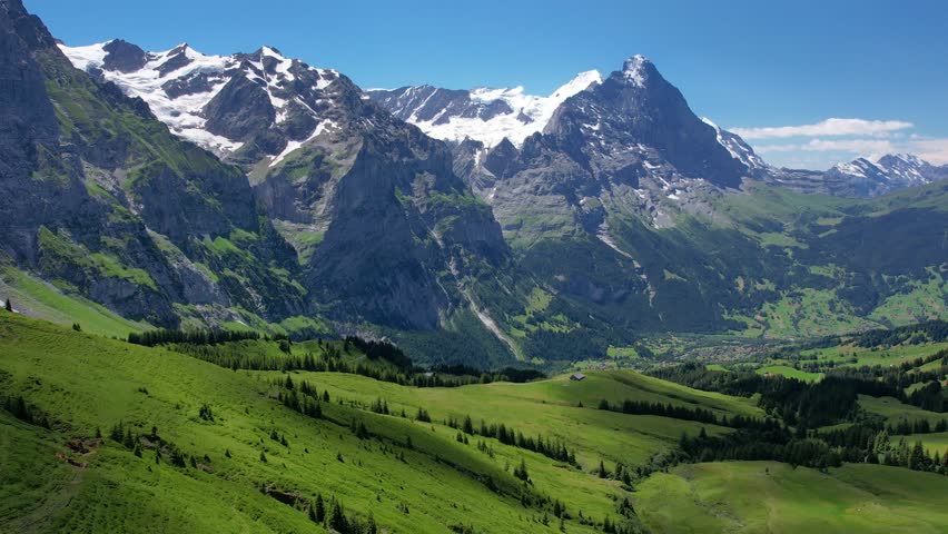 Cinematic drone fly over snow mountain and green meadows of tourist resort Grindelwald valley in Switzerland Bernese Alps. Travel and healthy lifestyle