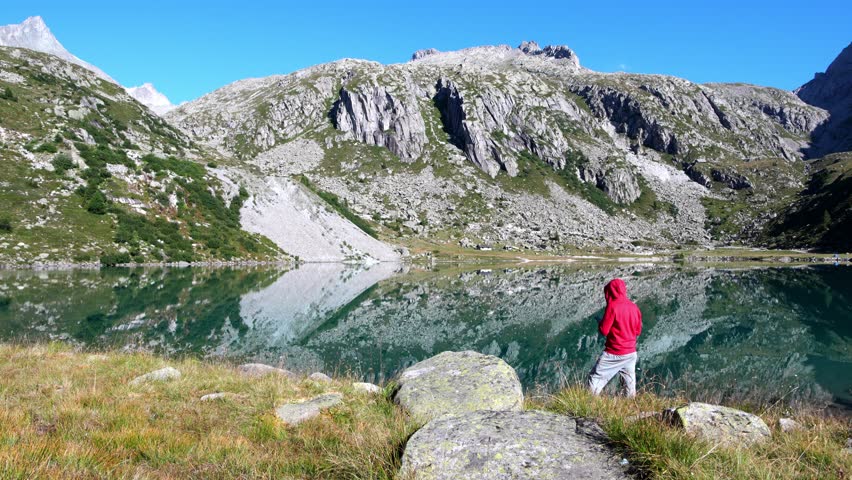 Boy with red sweatshirt meditates on the Dolomite lakes of Cornisello