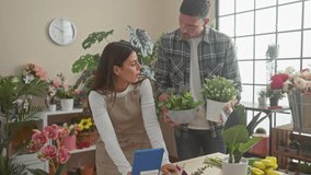 A woman florist uses a tablet while a man holds potted plants in a flower shop filled with various blooms and greenery. - Powered by Shutterstock - Get 15% off with code: PIKWIZARD15
