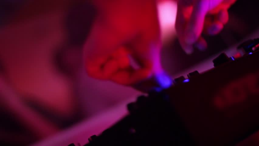 Dj hand tweaks controls of turntable mixer in nightclub (night club). Close-up