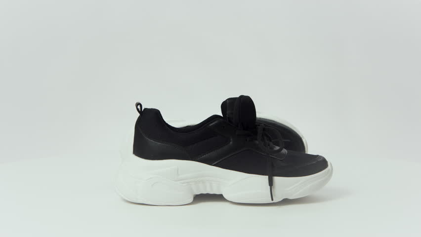 Unbranded black and white sneakers spin against a white backdrop, highlighting their sleek design. Perfect for sporty and outdoor adventures.