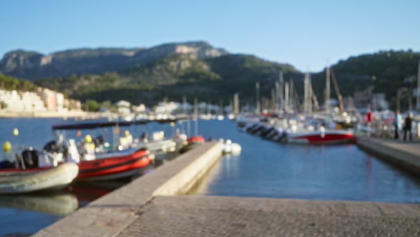 Blurred view of a busy marina with defocused boats and a picturesque mountain backdrop under a clear blue sky