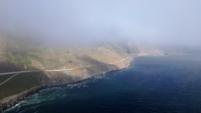 Stunning aerial drone shots beautifully capture Californias iconic Highway 1 winding through the rugged Big Sur coastline, enveloped in morning fog, creating a breathtaking and enchanting scenery