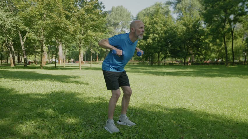 Motivated fit mature man in activewear practicing bent over dumbbell row workout , flexing and strengthening back, arm and shoulder muscles, building core stability during outdoor sports training