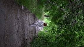 Vertical video of a young Asian woman in a white light dress, smiling, running along an alley of green trees - Powered by Shutterstock - Get 15% off with code: PIKWIZARD15