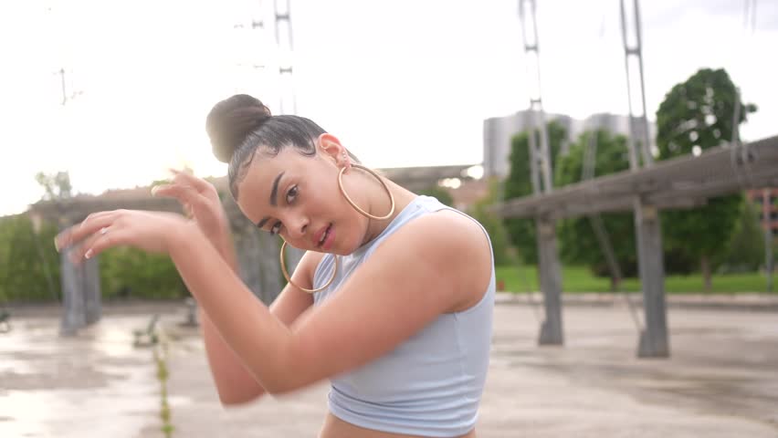 A woman is dancing on a concrete floor. She is wearing blue jeans and a blue shirt. Scene is energetic and fun