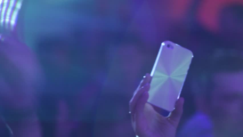 Phone in raised hand. Phone is filming the night club's atmosphere, people dance