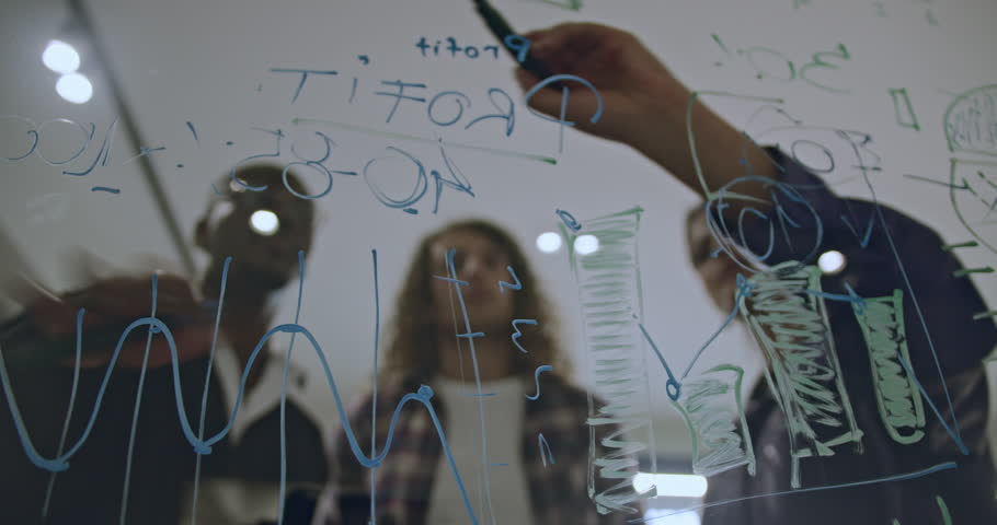 Multicultural colleagues brainstorm ideas together, writing on a glass board in a modern office, highlighting collaboration, teamwork, and strategic project planning.