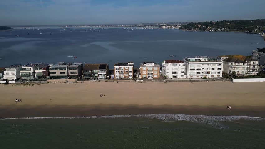 Sandbanks luxury houses on prime location by the sandy beach. Waterfront aerial view flying sideways. Pool Harbour in the background on a sunny morning in Dorset, UK.
