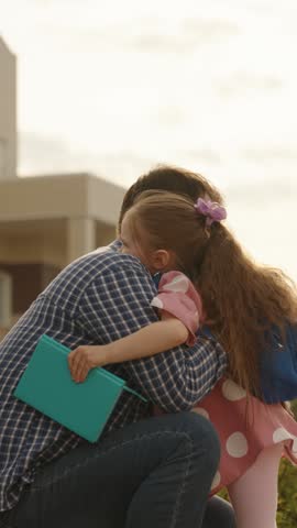 Happy family cute little daughter pupil and caring father embracing talking before primary school lesson outdoor. Smiling female kid child and dad hugging to each other going to elementary classroom