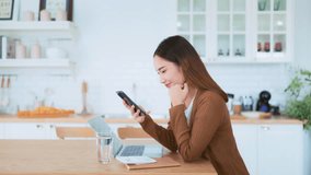 Happy young asian woman relax in domestic kitchen at home, using smartphone, smiling girl use cell phone chatting, browse wireless internet on gadget, shopping online from home - Powered by Shutterstock - Get 15% off with code: PIKWIZARD15