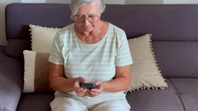 One senior woman using phone at home sitting on the couch to call parents or friends. Mature female compose number then call with cellular talking and enjoying communication. Lonely old lady indoor - Powered by Shutterstock - Get 15% off with code: PIKWIZARD15