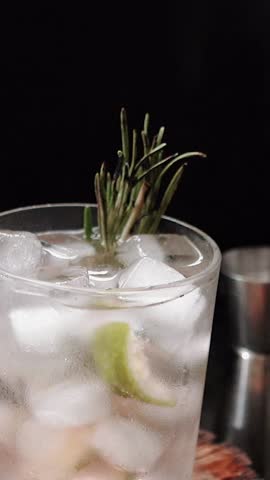 Close-up of rosemary being set on fire. The process of preparing a cocktail and a refreshing summer drink with alcohol for a party. Cold sparkling water with gin and lime