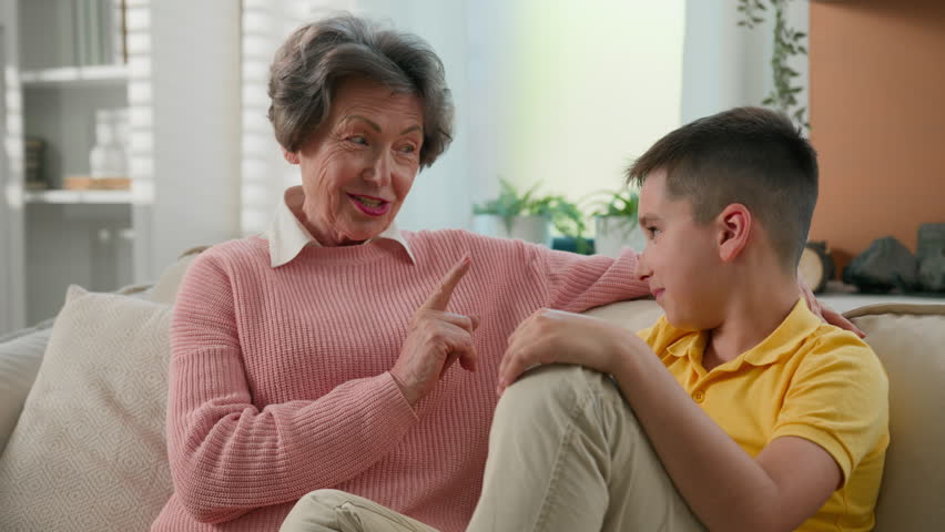 Caucasian grandmother explaining punishing spoiled grandson strict shaking index finger elderly caring woman grandma explain teaching discipline grandchild child kid boy on couch at home happy family