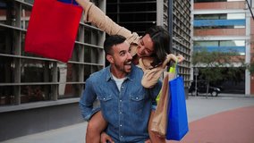 A smiling man carries his girlfriend piggyback while she holds shopping bags as they head to buy gifts at a store in the mall. Young couple having fun bonding on the sale day. Lovely customers buying - Powered by Shutterstock - Get 15% off with code: PIKWIZARD15