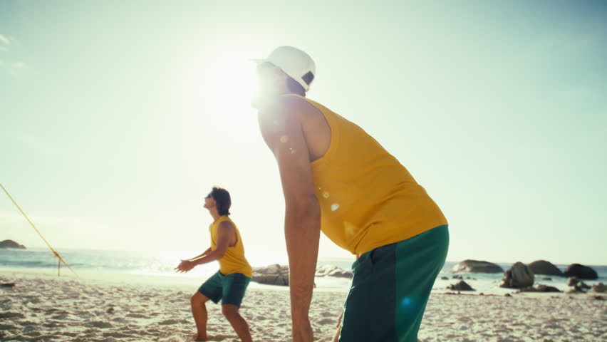 A dynamic handheld shot of two male beach volleyball players displaying teamwork on beach volleyball court. They shake hands after a successful teamwork point.