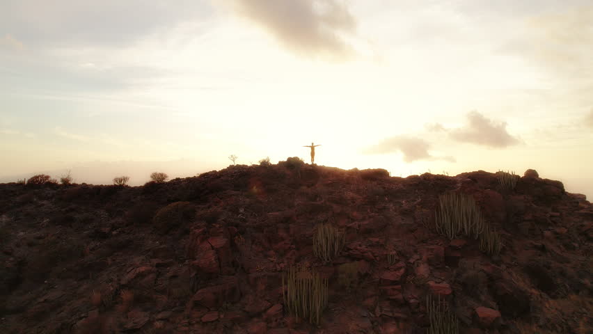 Person with arms outstretched standing on the peak of Los Gigantes Cliffs during sunset with a dramatic sky. Tenerife Canary Islands Spain.