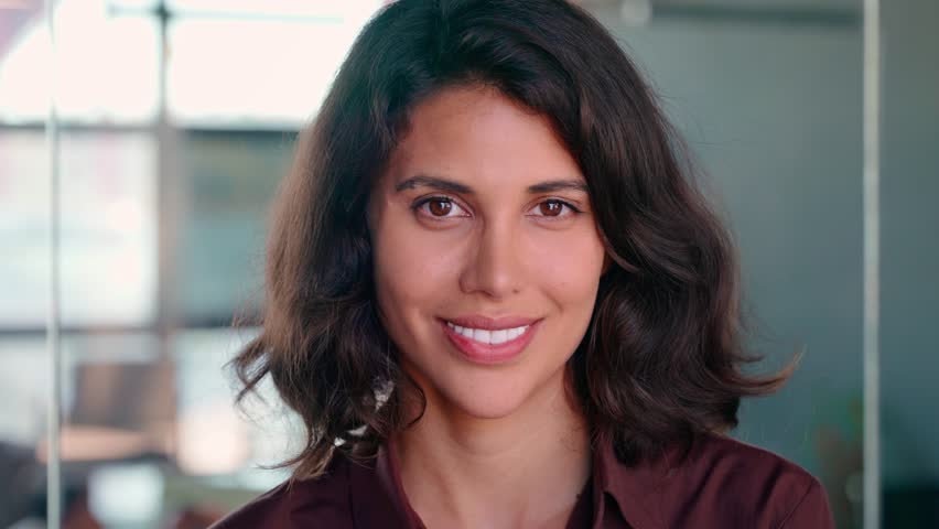 Closeup headshot face portrait of beautiful successful hispanic young business woman looking confident at camera. Smiling latin or eastern middle age female ceo leader businesswoman standing in office
