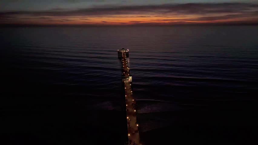 Aerial Drone Video of Oceanside California Pier during a sunset. This video at dusk is shot from way up high showing a calm ocean and red colored skies.