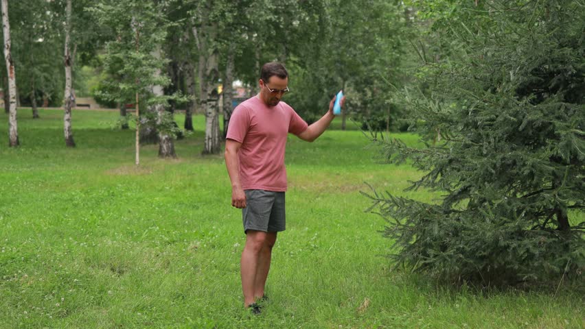 a man sprays protective repellent on his skin and clothes while walking in the park
